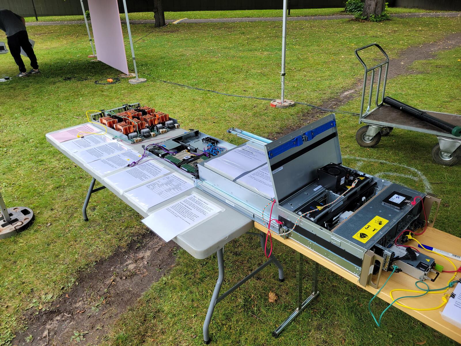 The dgx04 booth outdoors at Aalto Day One 2025, with the disassembled server and printed info sheets laid out on a table
