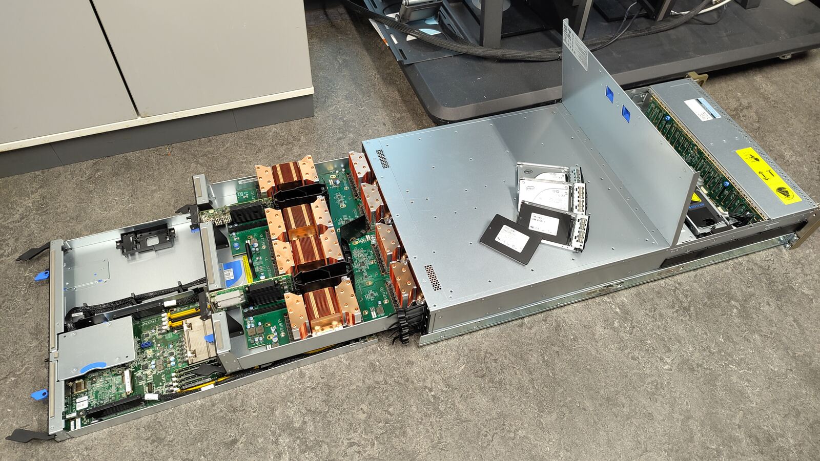 The dgx04 server disassembled on a table, showing its motherboard tray, copper GPU heatsinks, and drives